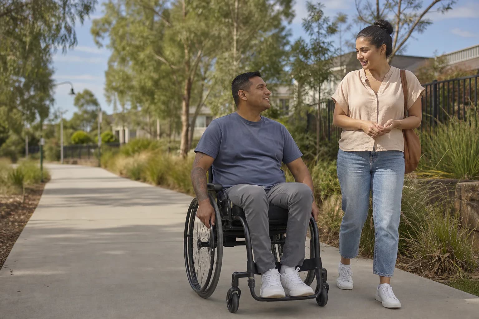 Illustrative image of an adult wheelchair user and a support worker talking on an accessible community path.